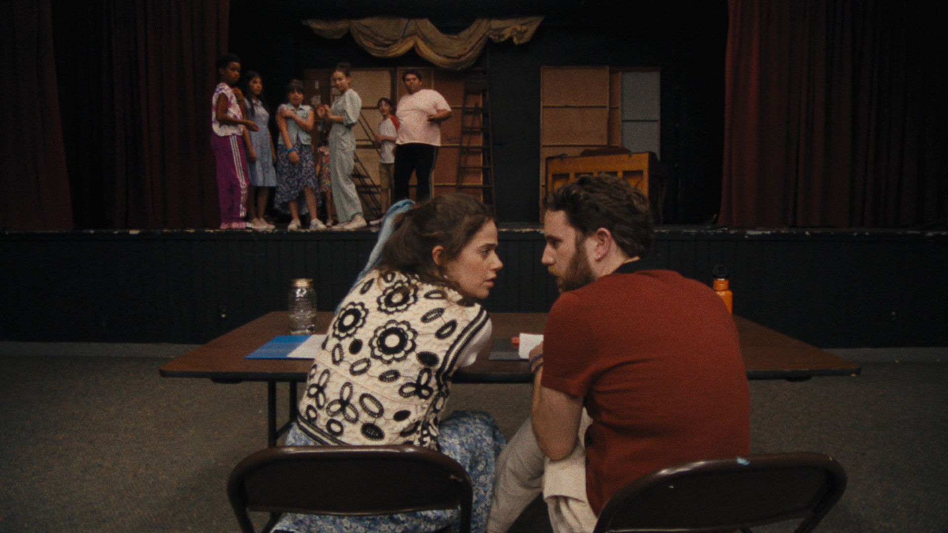 A photo of a man and a woman sitting on chairs in front of a theater stage